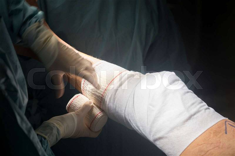 Nurse bandaging after knee surgery hospital operation medical procedure in emergency room operating theater, stock photo