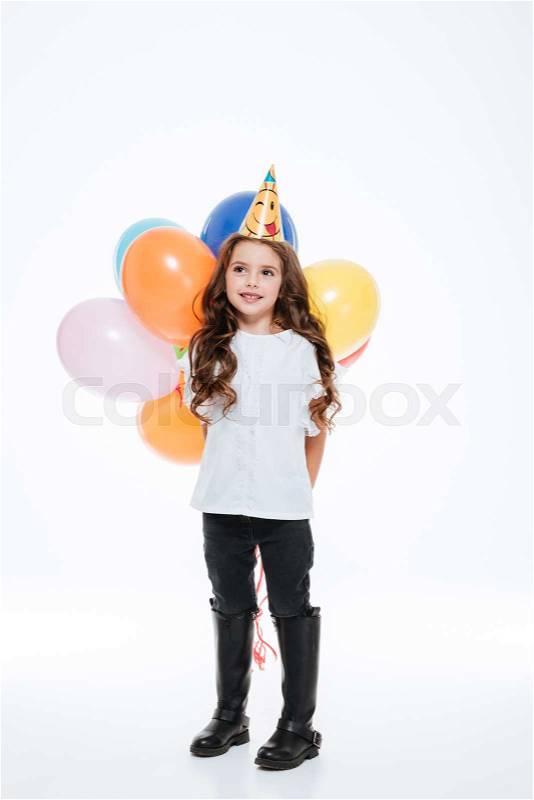 Little girl in birthday hat holding colorful balloons behind her, stock photo