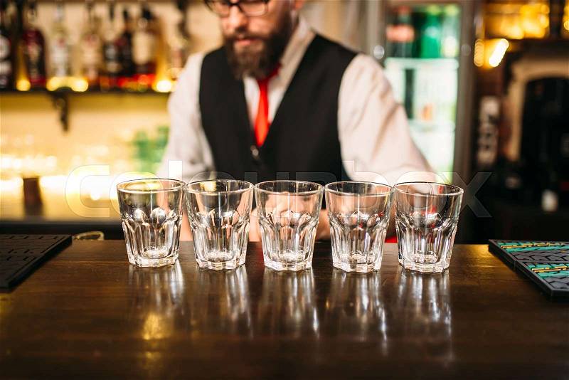 Empty glasses on wooden bar counter, bartender working on background, stock photo