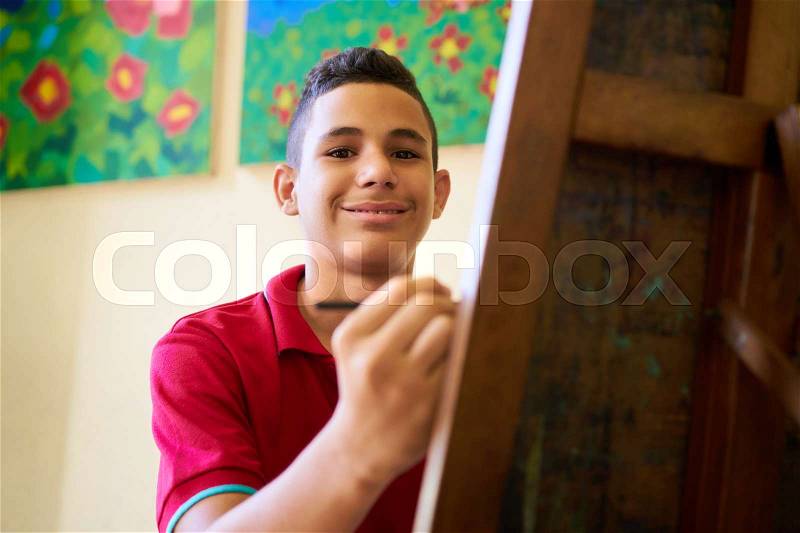 School of art, college of arts. Portrait of happy latin american boy smiling, learning to paint and looking at camera, stock photo