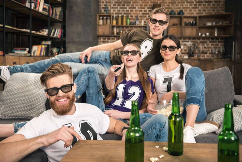 Happy young friends in 3D glasses watching movie on sofa at home , stock photo
