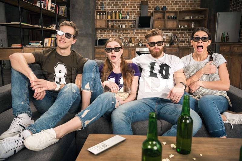 Young friends in 3D glasses watching movie with beer at home, stock photo
