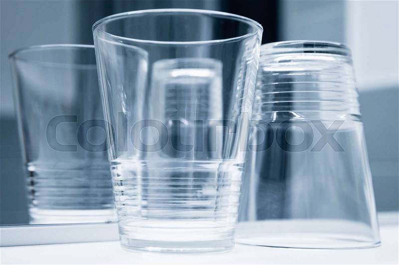 Empty glasses stand on white shelf near the mirror, blue toned closeup photo, stock photo