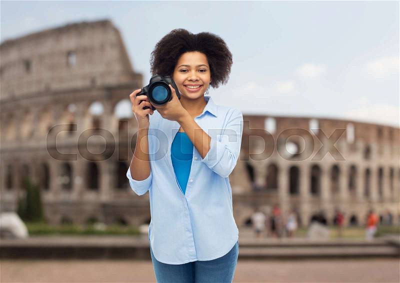 Travel, tourism, people and photography concept - happy african american young woman with digital camera over coliseum background, stock photo