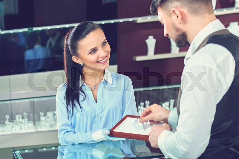 Advising her client. Professional jewelry store clerk smiling joyfully showing precious diamond ring to her customer profession positivity working jewelry bridal choosing buying engagement concept , stock photo