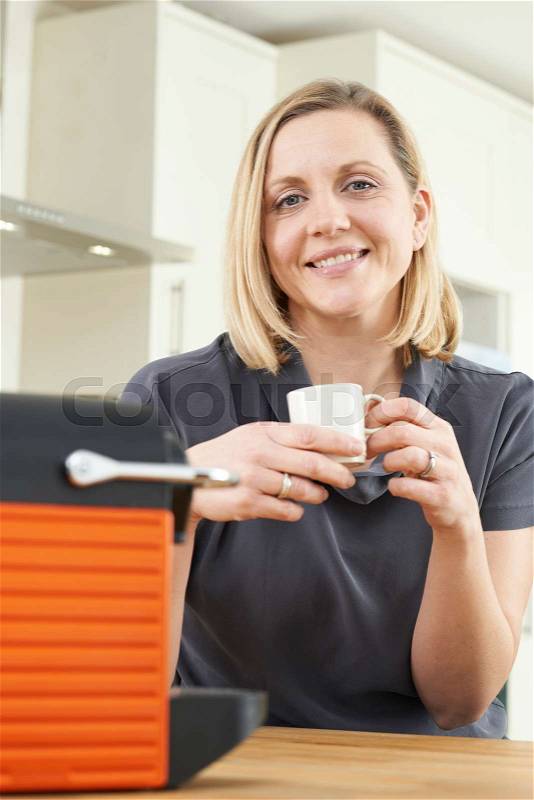 Woman Using Coffee Capsule Machine In Kitchen, stock photo