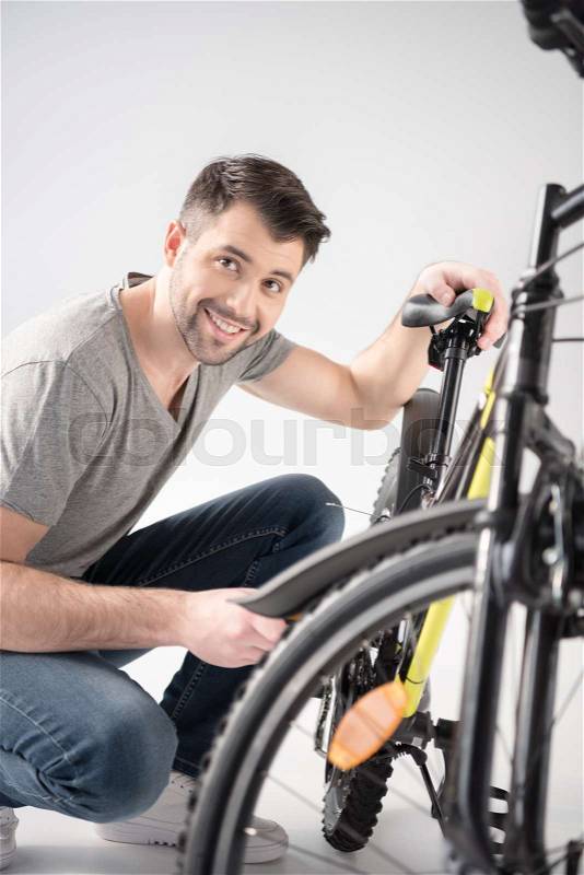 Young handsome man crouching while checking bicycle and smiling at camera, stock photo
