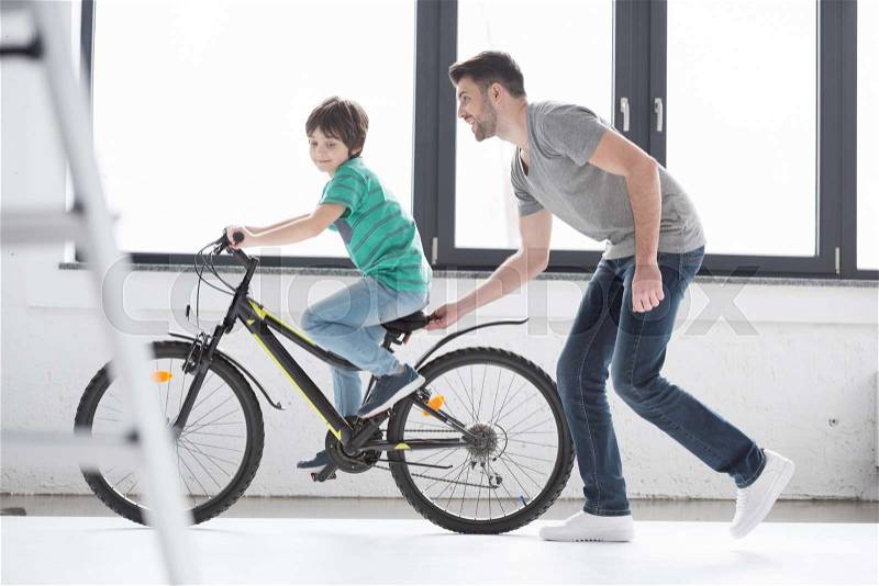 Side view of young father helping son to ride bicycle, stock photo