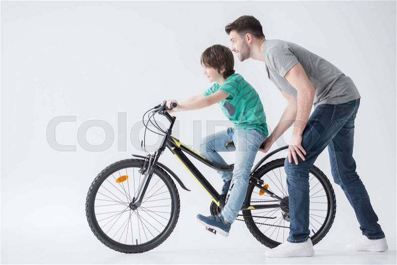 Side view of father helping son to ride bicycle on white, stock photo