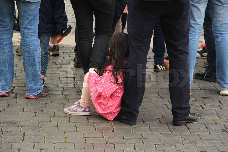 The little girl in striking pink raincoat is sitting on the foot of her father in the centre of the city in the summer, stock photo