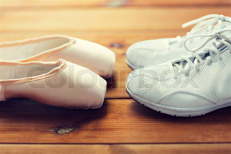 Sport, ballet, fitness, footwear and objects concept - close up of sneakers and pointe shoes on wooden floor, stock photo