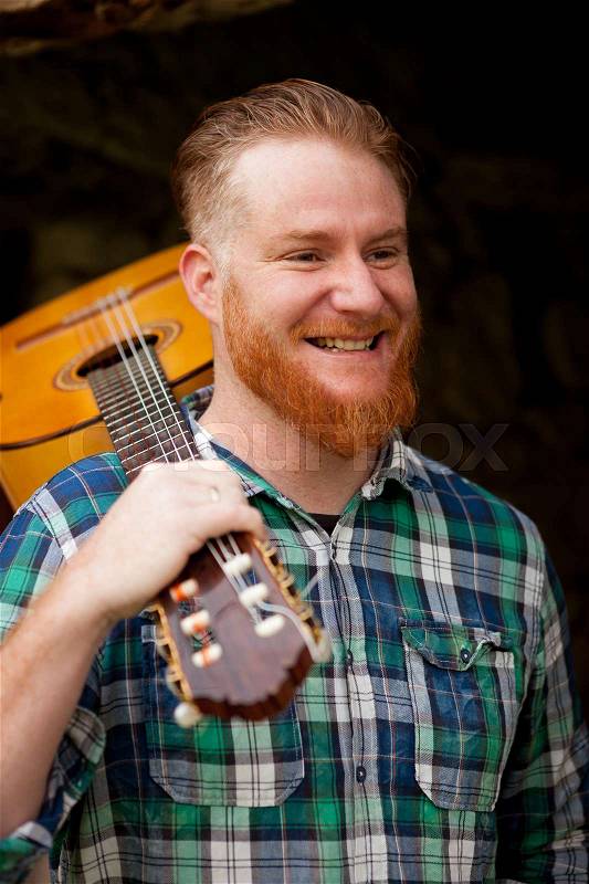 Hipster man with red beard holding a guitar in a rustic house, stock photo