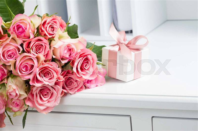 Gift box with pink ribbon with rose flowers on white table, stock photo