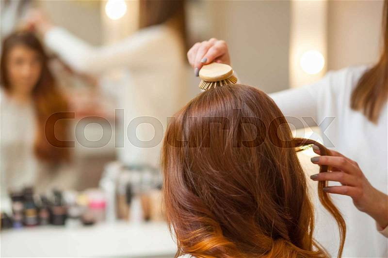Hairdresser combing her long, red hair of his client in the beauty salon. Professional hair care and creating hairstyles, stock photo