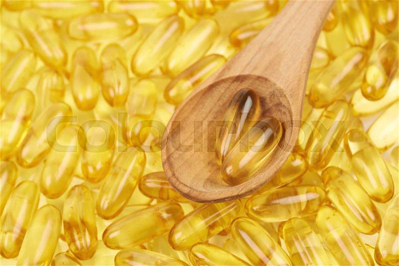 Surface covered with multiple yellow softgel pills with a wooden spoon over it as a medical backdrop composition, stock photo