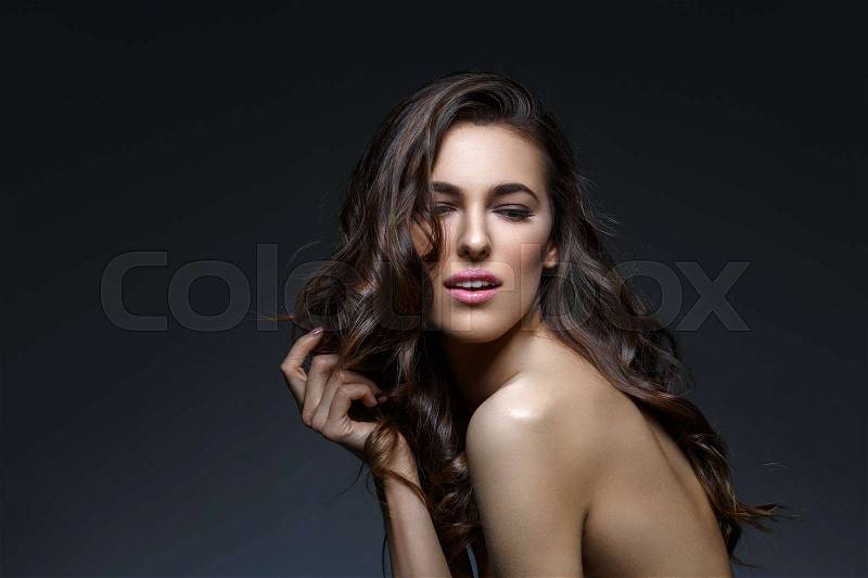 Beautiful brunette young woman with long healthy thick wavy hair and make-up on black background. Copy space, stock photo