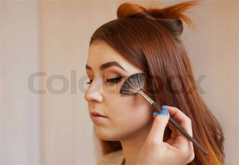 Makeup artist applied with a brush blush on the girl\'s face, concludes the daily make-up in a beauty salon. Professional skin care, stock photo