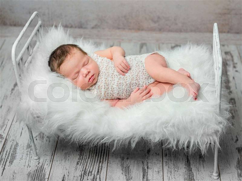 Cute sleeping newborn baby on cot with white fluffy blanket in studio, stock photo