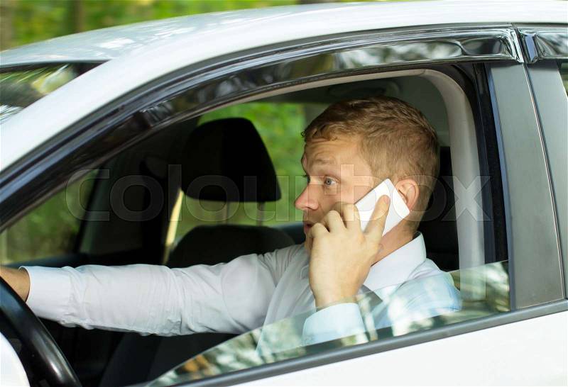 Young man talking on the phone behind the wheel of a car, creating an emergency situation, stock photo