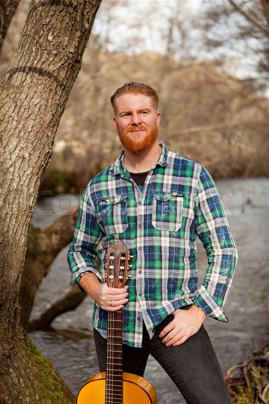 Hipster man with red beard with a guitar in the field, stock photo