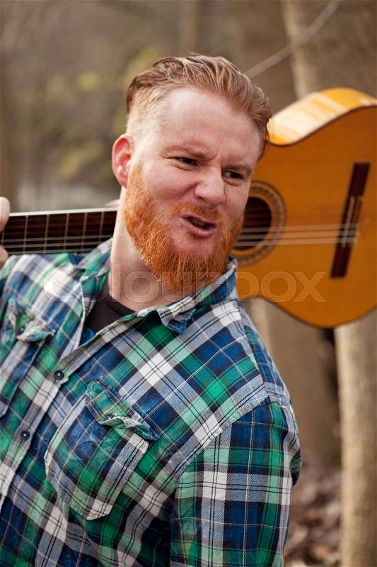 Hipster man with red beard holding a guitar in the field, stock photo