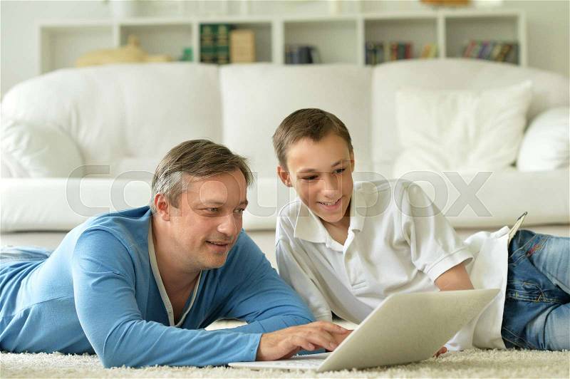 Son and father using laptop at home, stock photo