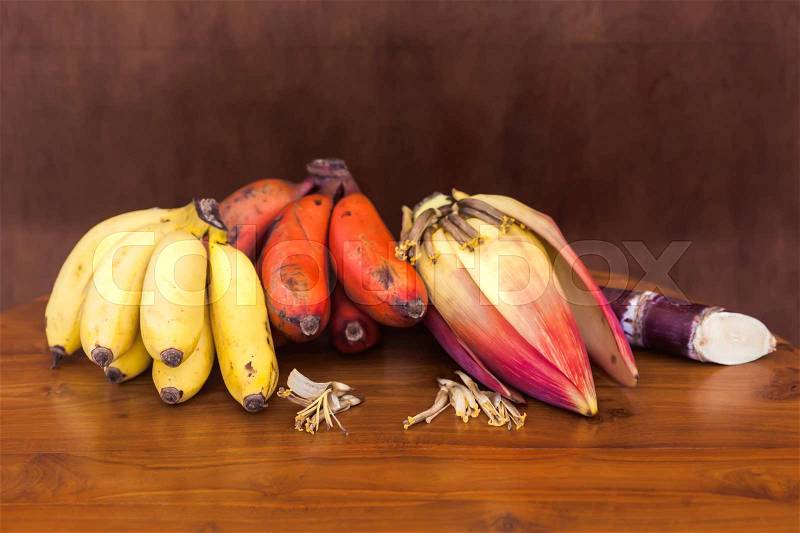 Fresh red and yellow banana bunches and unripe banana on wooden table on wooden brown wall, stock photo