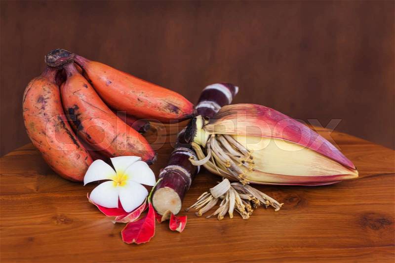 Fresh red banana and unripe banana bunches on wooden table on wooden brown wall, stock photo