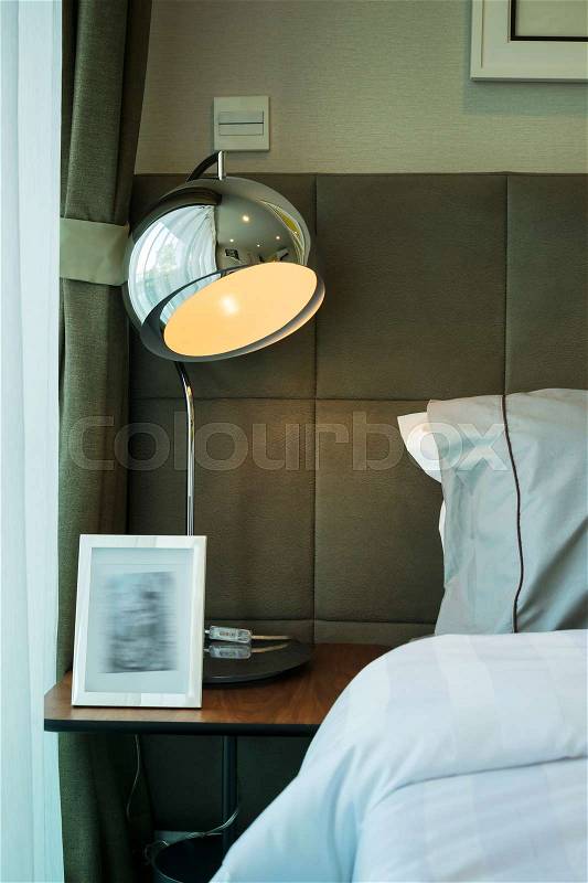 Metal desk lamp and grey pillow on bed, stock photo