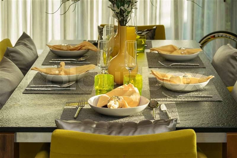 Dining table and comfortable yellow chairs in modern home with elegant table setting, stock photo