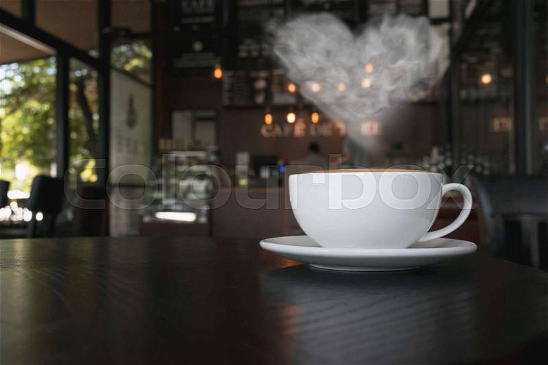Coffee cup on the table at the coffee shop with heart shaped smoke vintage color tone, stock photo