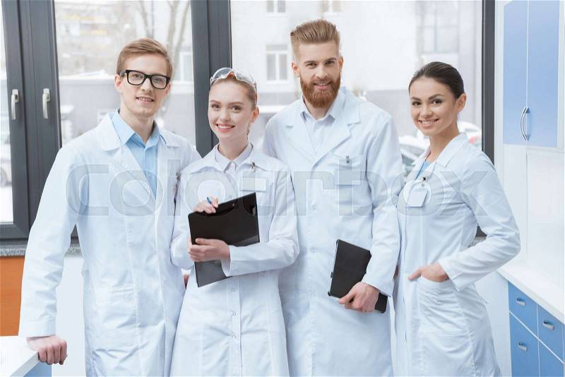 Team of young professional scientists in white coats smiling at camera in laboratory , stock photo