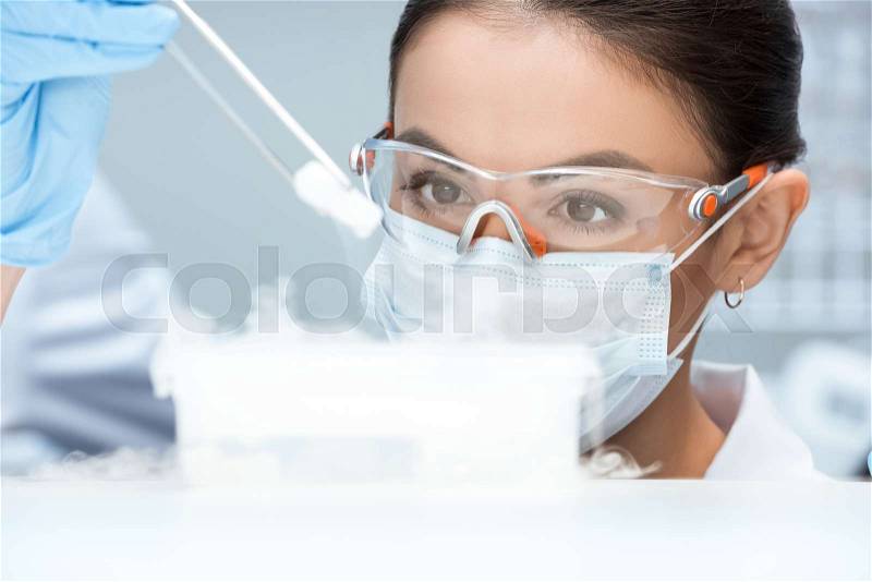Young woman scientist in protective goggles and mask making experiment in laboratory , stock photo