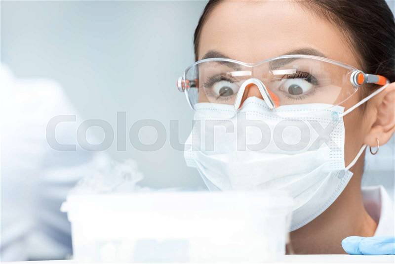 Shocked woman chemist in protective goggles and mask making experiment in laboratory , stock photo