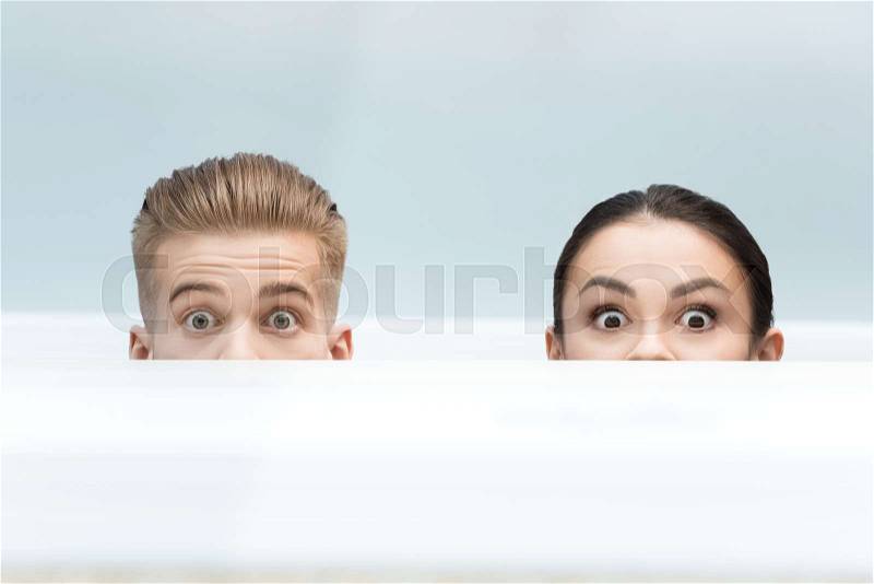 Partial view of scared scientists looking out behind table in lab, stock photo