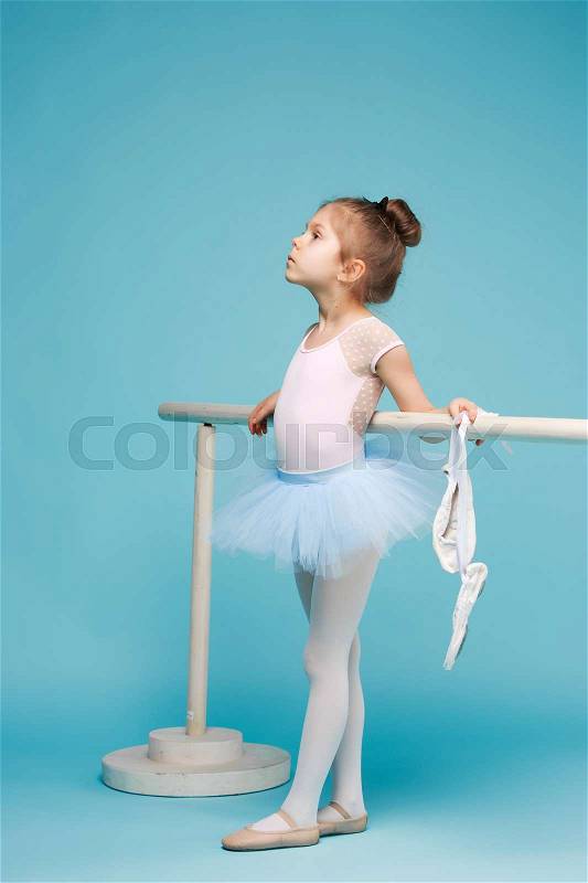 The little girl as balerina dancer posing near ballet rack on blue studio background, stock photo