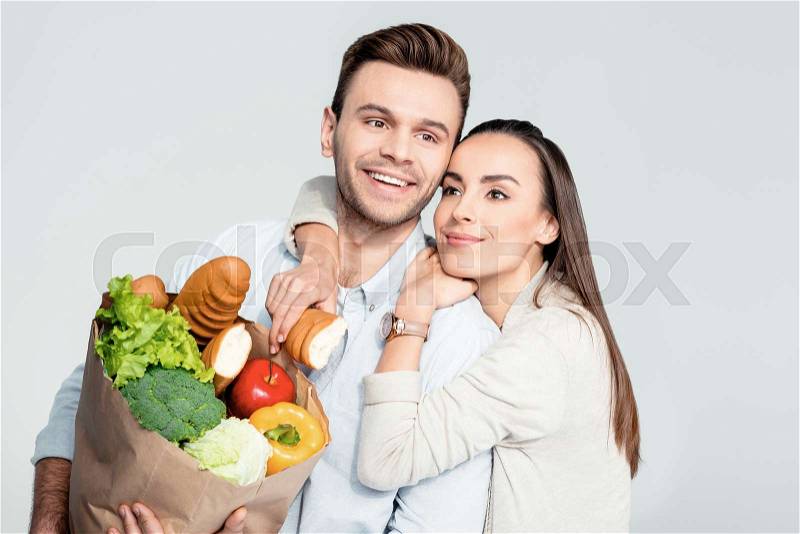Portrait of happy woman hugging man with grocery bag and looking away, stock photo