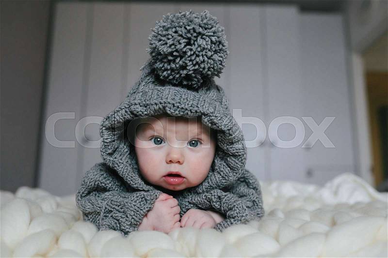 Small baby in knitted clothes lying in the room, stock photo