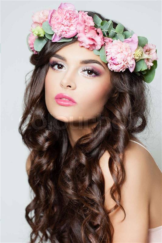 Beautiful Model with Long Curly Hair, Fashion Makeup and Summer Pink Flowers. Young Woman with Flowers Hairstyle, stock photo
