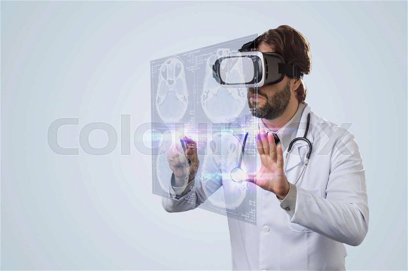 Male doctor on a gray background, using a Virtual Reality Glasses, looking at a virtual Screen, stock photo
