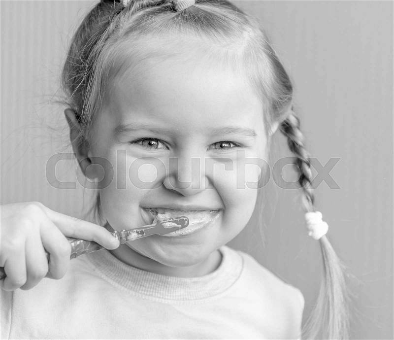Little girl with a funny hairstyle brushing her teeth and smiling widely, happy and emotional, stock photo