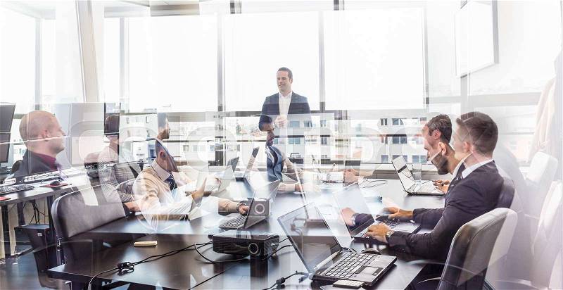 Successful team leader and business owner leading informal in-house business meeting. Business people working on laptops in foreground and glass reflections. Business and entrepreneurship concept, stock photo