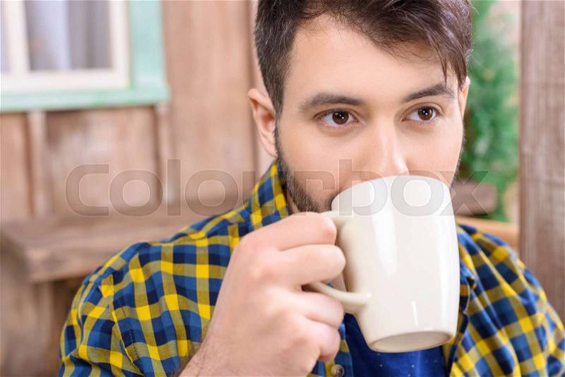 Portrait of man drinking tea on porch and looking away, stock photo