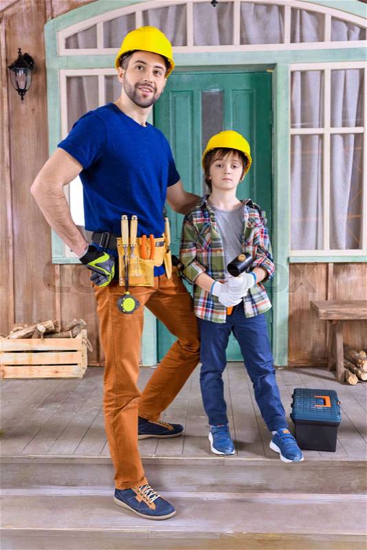 Father and son in helmets with building tools standing on porch , stock photo