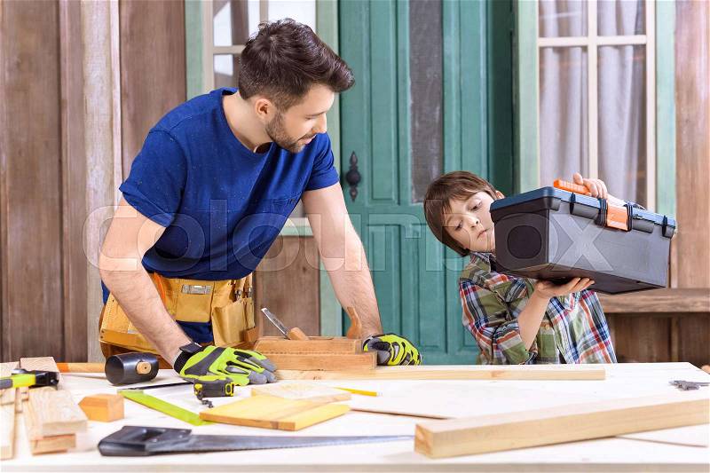 Portrait of son helping father working with wooden planks on porch, stock photo