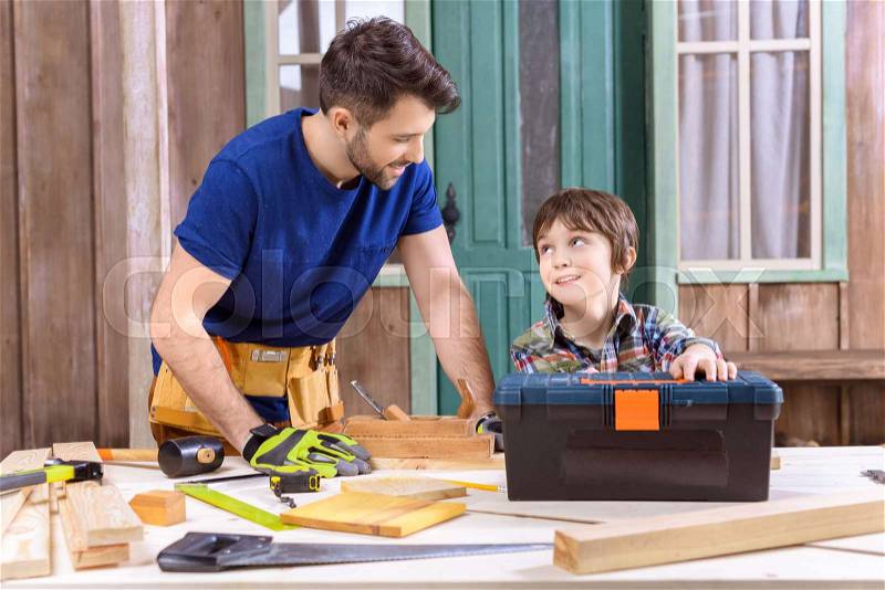 Portrait of son helping father working with wooden planks on porch, stock photo