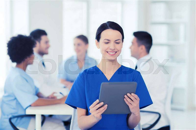 Clinic, profession, people and medicine concept - happy female doctor with tablet pc computer over group of medics meeting at hospital, stock photo