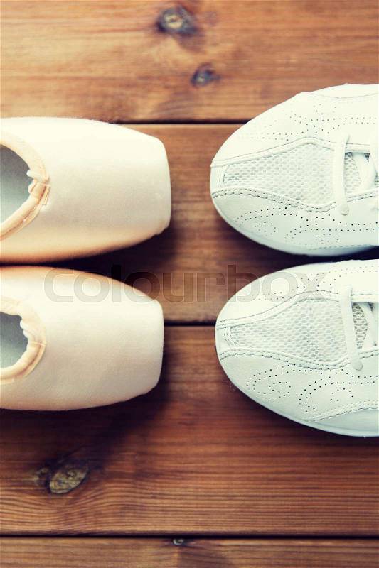 Sport, ballet, fitness, footwear and objects concept - close up of sneakers and pointe shoes on wooden floor, stock photo