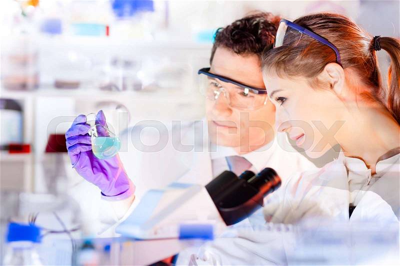 Life science researchers observing solution in laboratory. Chemical lab. Attractive young PhD student and her post doctoral supervisor scientist observing blue indicator color shift after in flask, stock photo