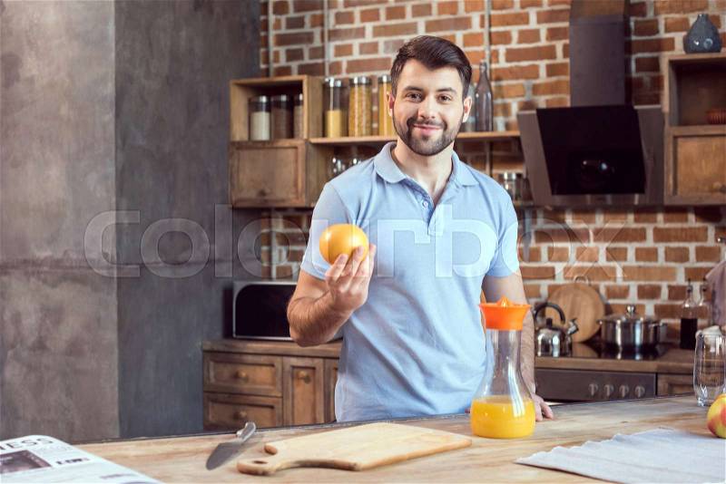 Handsome young smiling man squeezing fresh juice in kitchen, stock photo